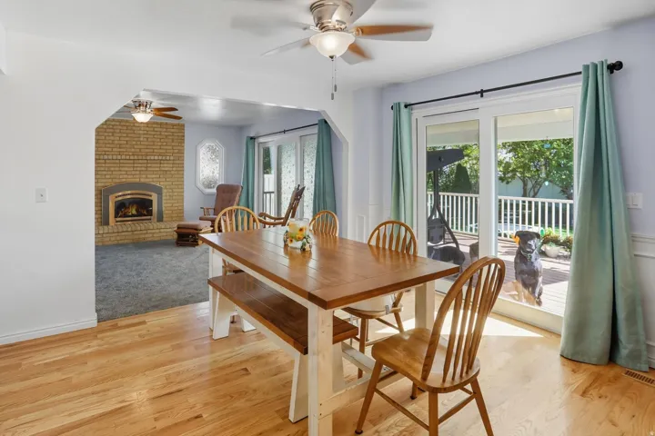 Dining area featuring a ceiling fan, a brick fireplace, light wood-style flooring, and a wainscoted wall