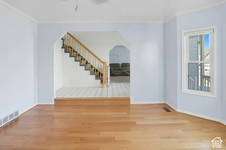 Empty room featuring light wood-style floors, ornamental molding, and arched walkways