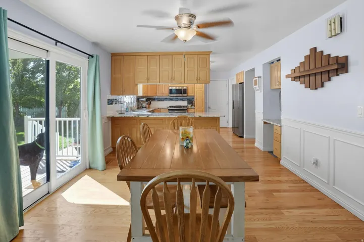 Dining room with light wood-type flooring, ceiling fan, a wainscoted wall, and a decorative wall