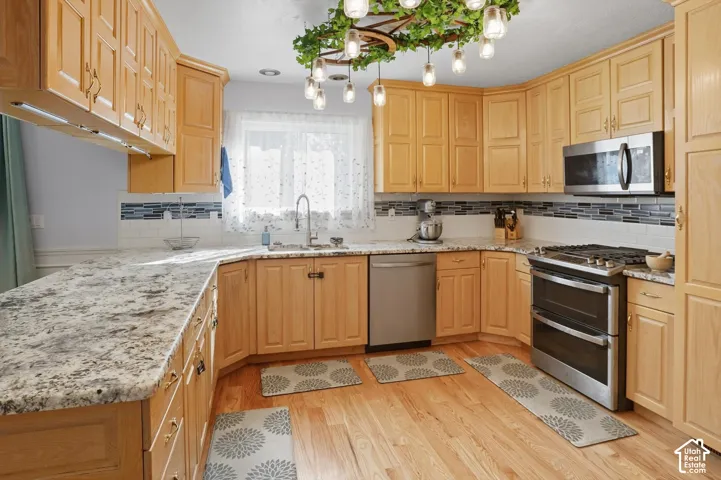 Kitchen featuring stainless steel appliances, light stone counters, light wood finish cabinets, light wood-style flooring, and backsplash