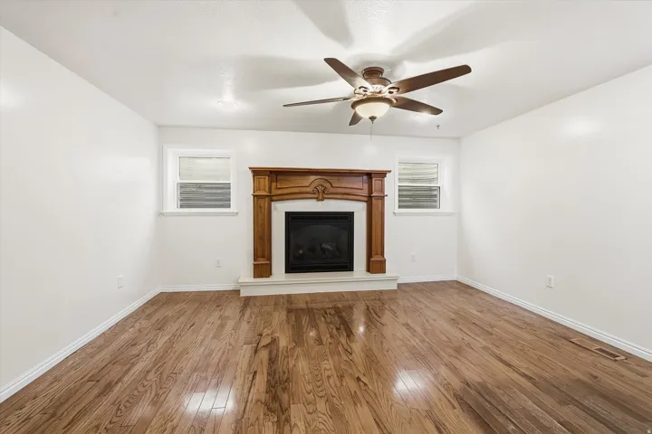 Unfurnished living room featuring wood-type flooring, ceiling fan, plenty of natural light, and a fireplace with raised hearth