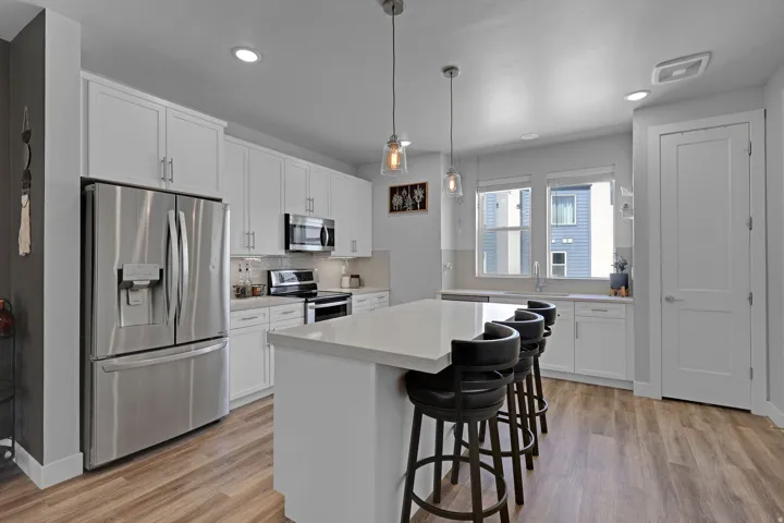 Kitchen featuring stainless steel appliances, white cabinets, a center island, a breakfast bar, and decorative light fixtures