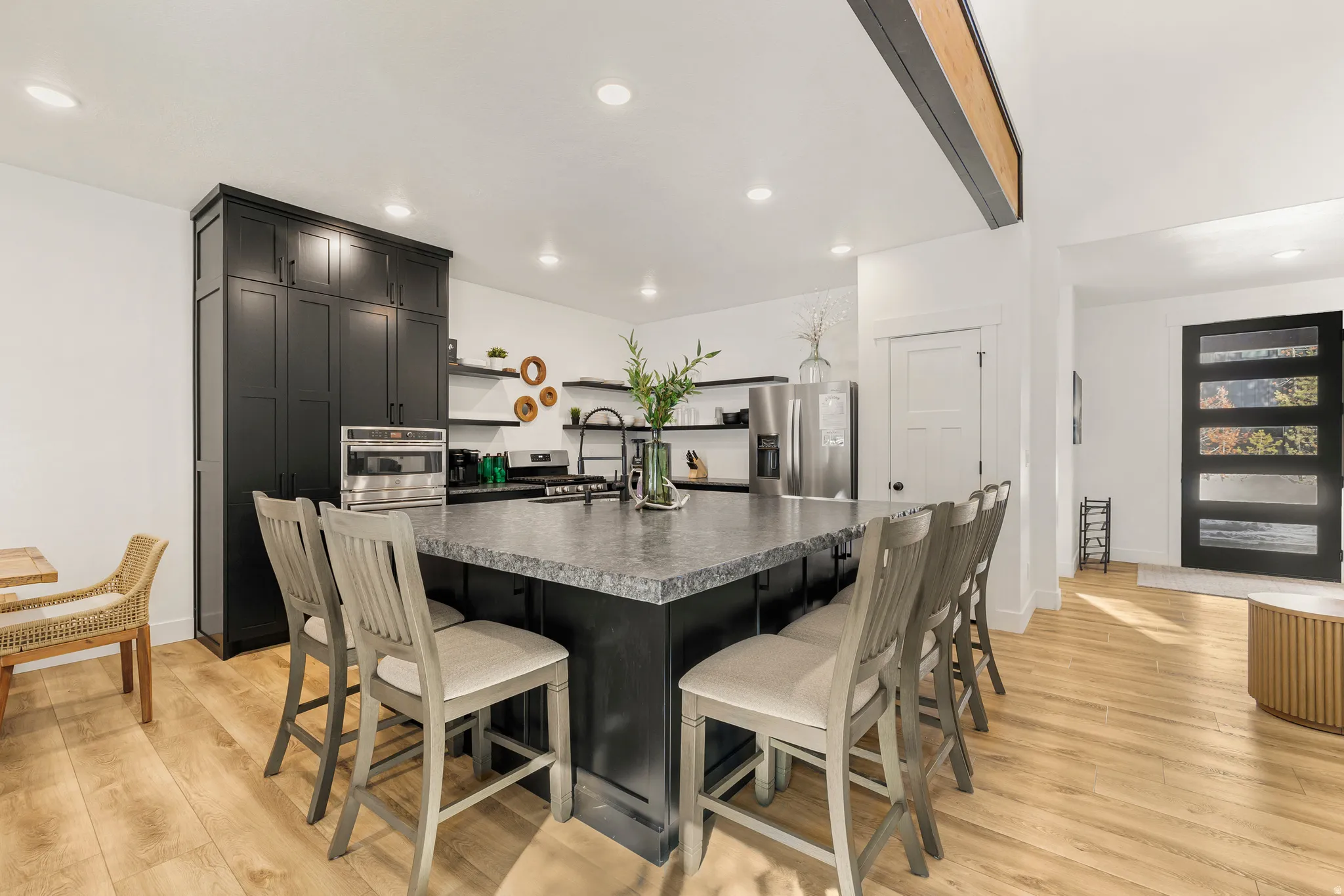 Kitchen with dark cabinets, a kitchen island with sink, a kitchen breakfast bar, stainless steel fridge, and beamed ceiling