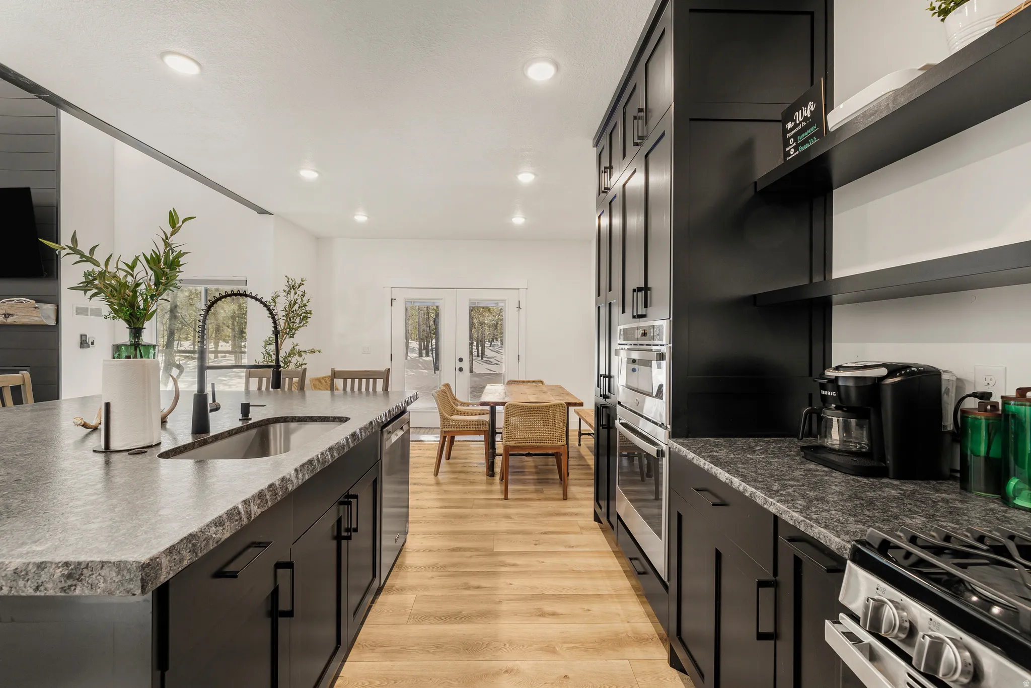 Kitchen featuring dark cabinetry, stainless steel appliances, open shelves, light wood-type flooring, and recessed lighting