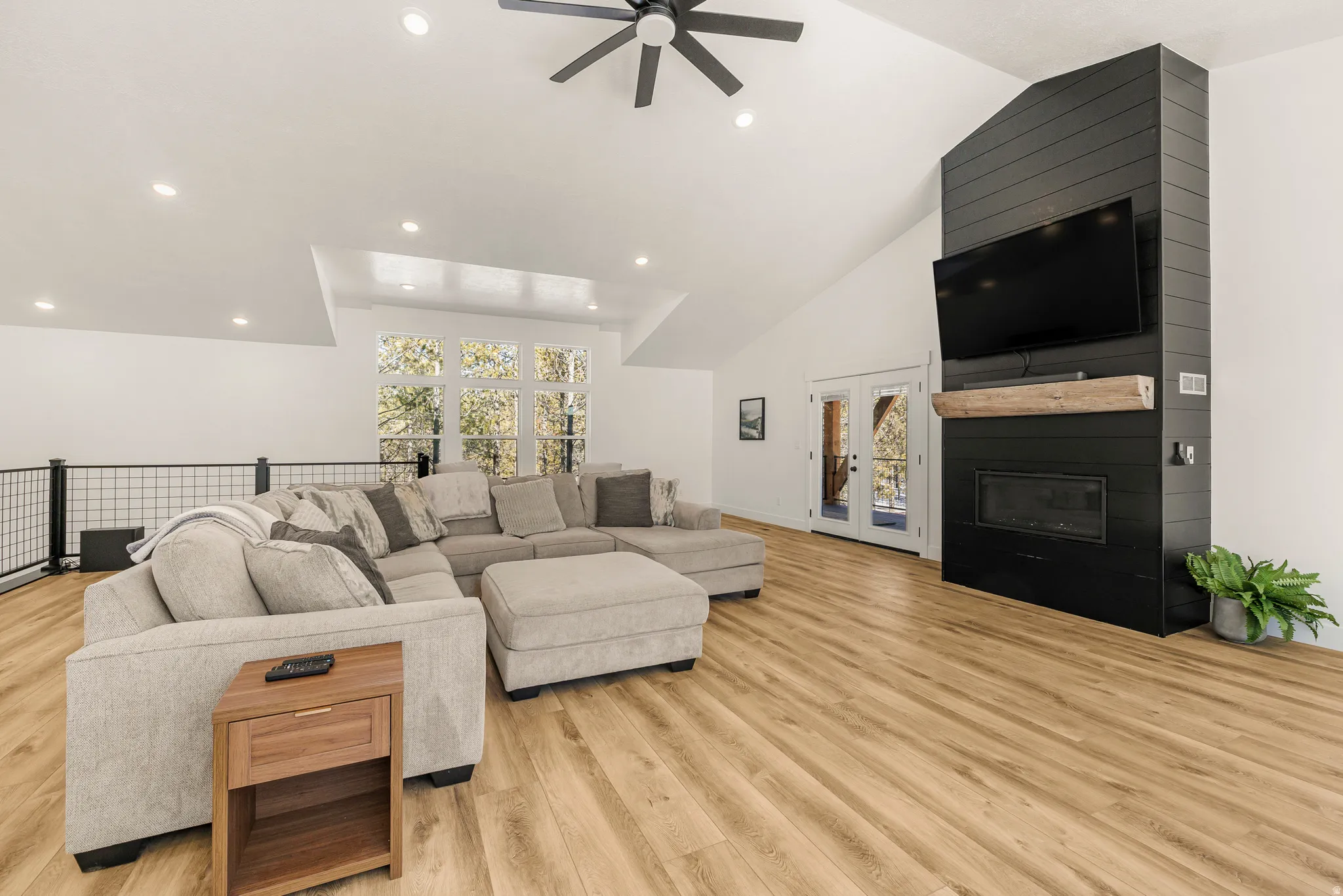 Living area with ceiling fan, vaulted ceiling, light wood-style flooring, a large fireplace, and recessed lighting