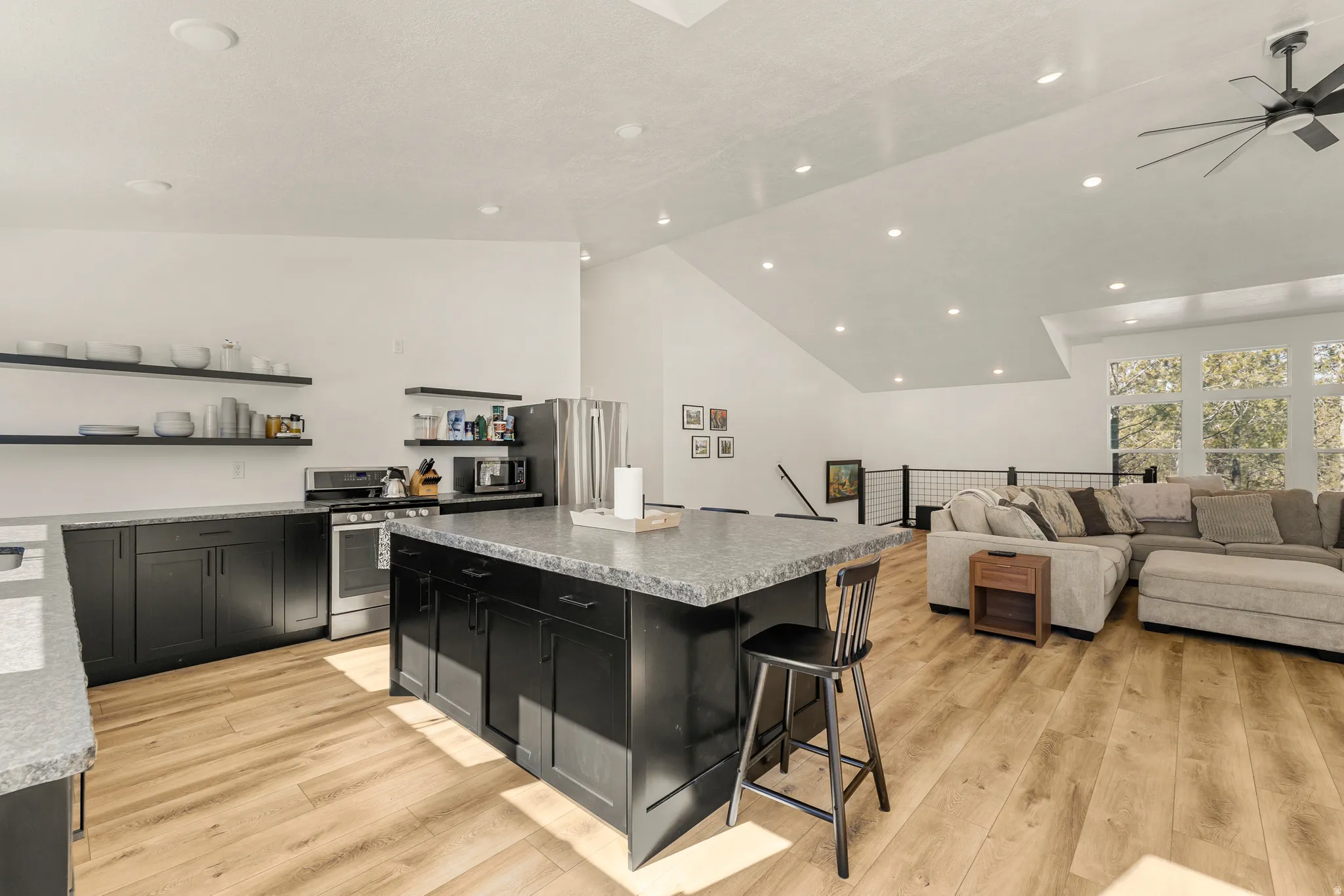 Kitchen featuring stainless steel appliances, lofted ceiling, a kitchen bar, a center island, and dark cabinets