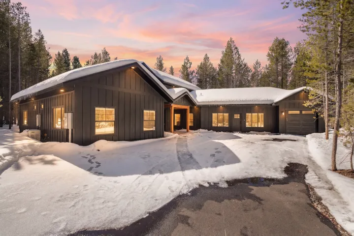 View of front facade featuring board and batten siding, a garage, roof mounted solar panels, and driveway