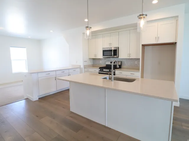 Kitchen featuring a peninsula, white cabinetry, stainless steel appliances, dark wood-style floors, and pendant lighting