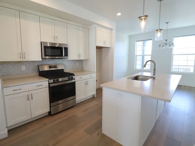 Kitchen with stainless steel appliances, white cabinets, tasteful backsplash, dark wood-style floors, and a kitchen island with sink