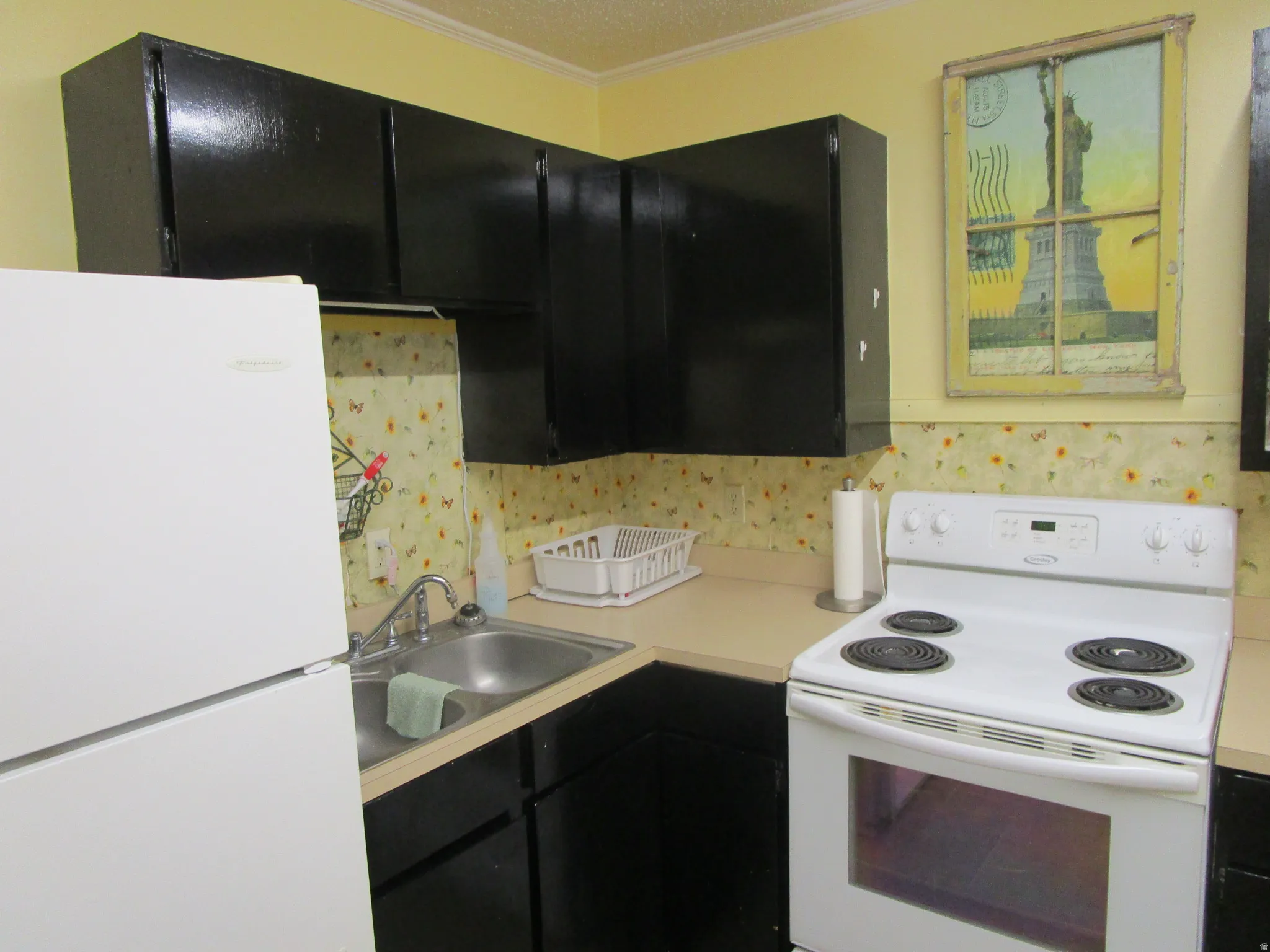 Kitchen with dark cabinetry, white appliances, light countertops, and crown molding