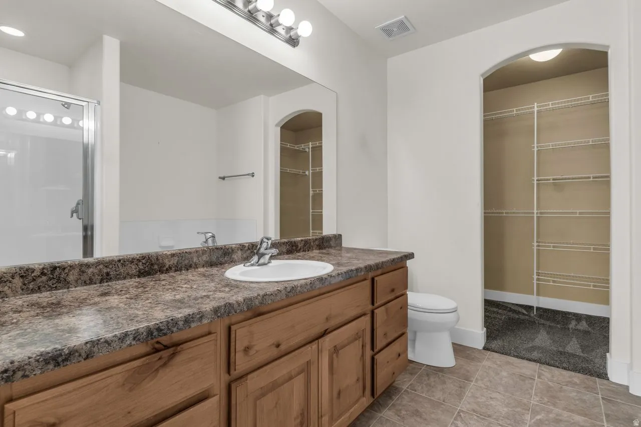 Full bath with vanity, a stall shower, a spacious closet, and light tile patterned flooring