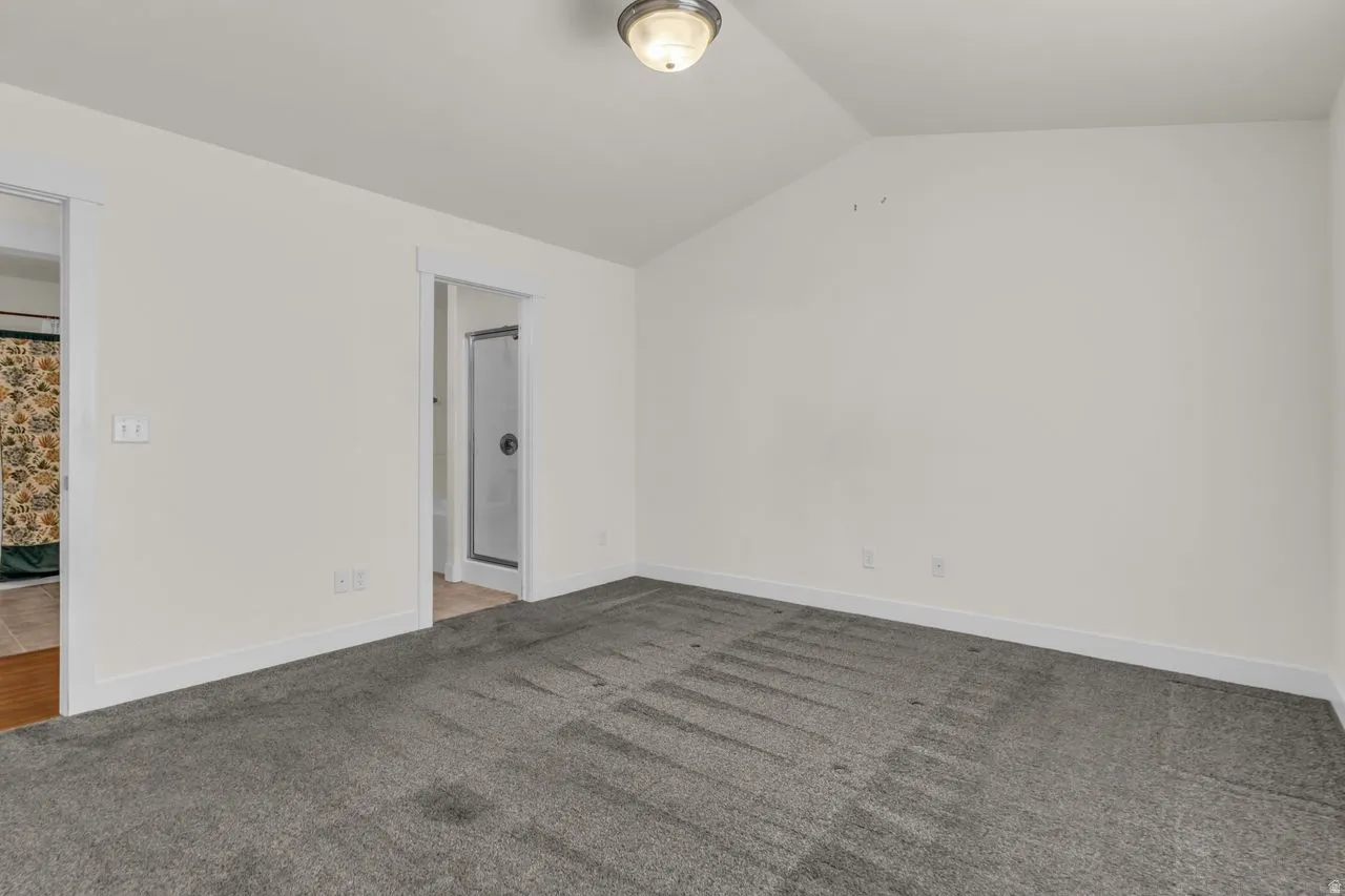 Carpeted spare room with vaulted ceiling and baseboards