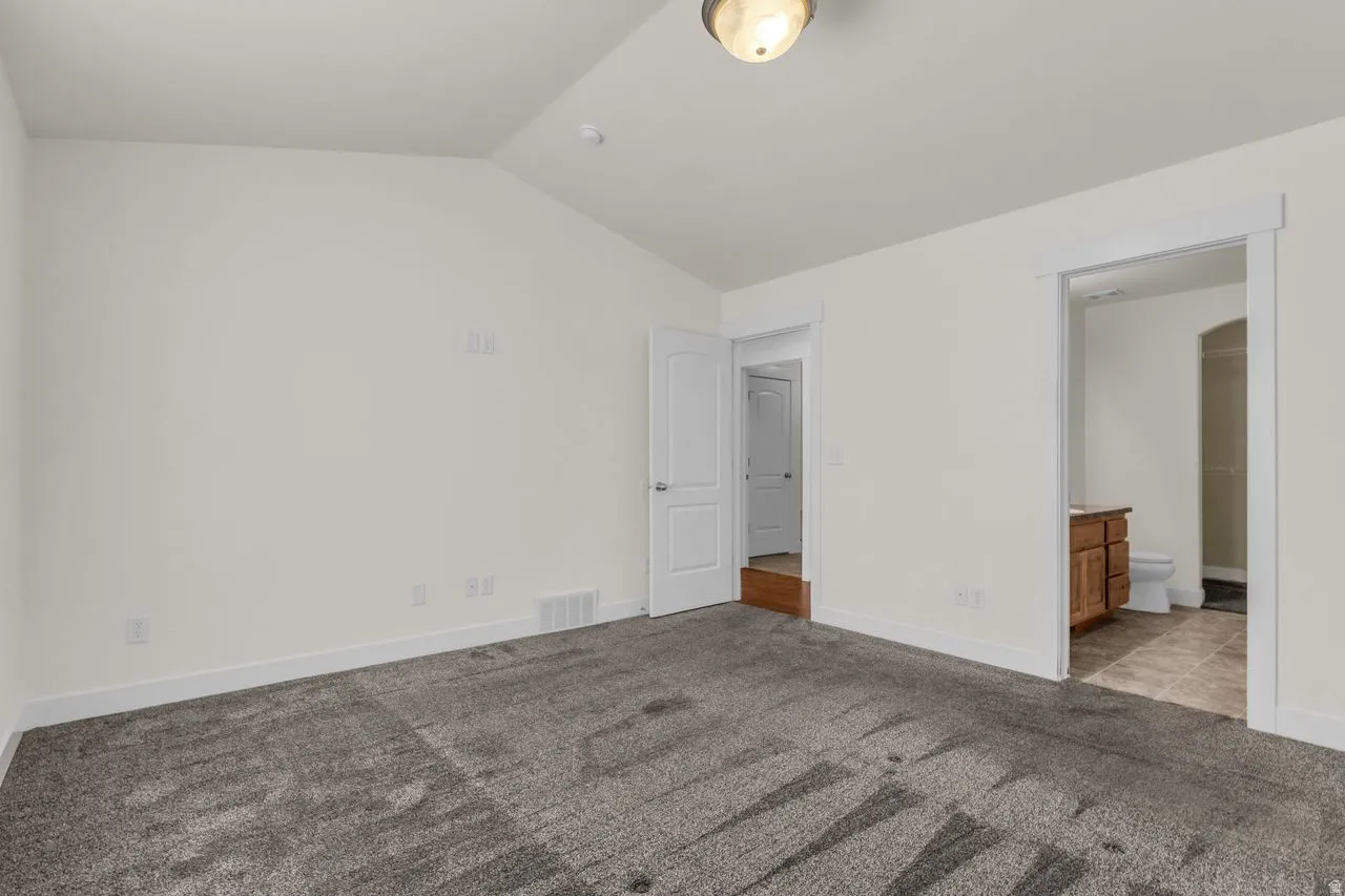 Unfurnished bedroom featuring dark carpet, vaulted ceiling, and ensuite bathroom