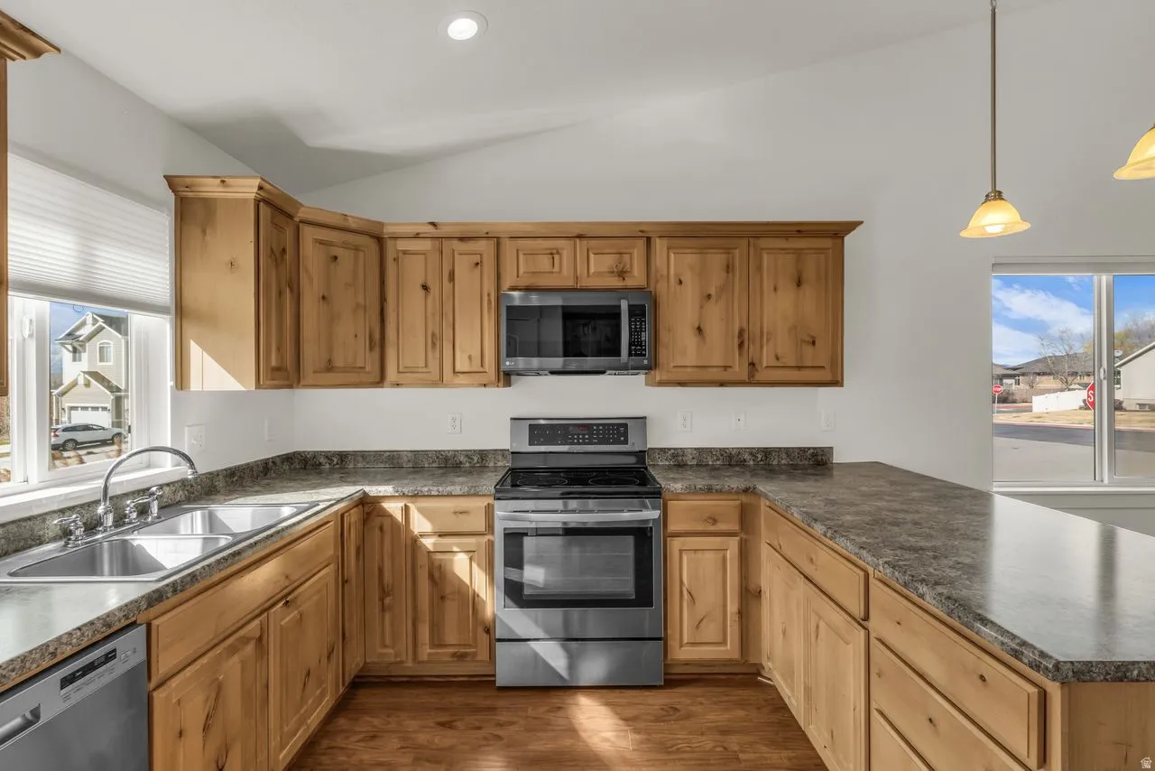 Kitchen featuring stainless steel appliances, dark countertops, lofted ceiling, dark wood finished floors, and a peninsula