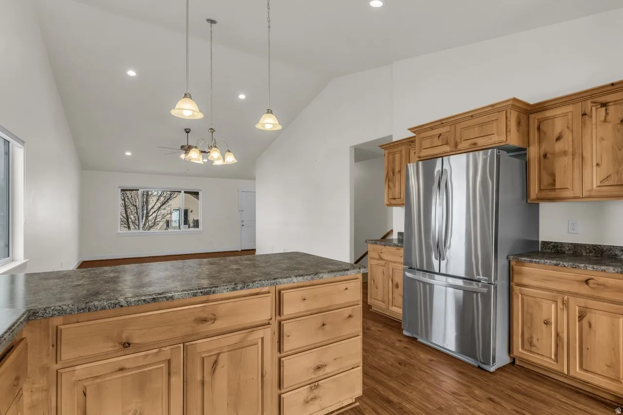 Kitchen featuring freestanding refrigerator, dark countertops, lofted ceiling, dark wood-style flooring, and a ceiling fan