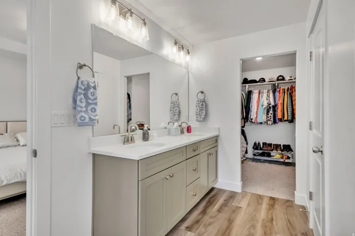 Ensuite bathroom with double vanity, light wood-type flooring, and a spacious closet