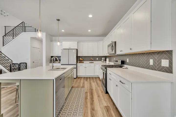Kitchen featuring stainless steel appliances, light wood-style flooring, a breakfast bar area, decorative light fixtures, and white cabinets
