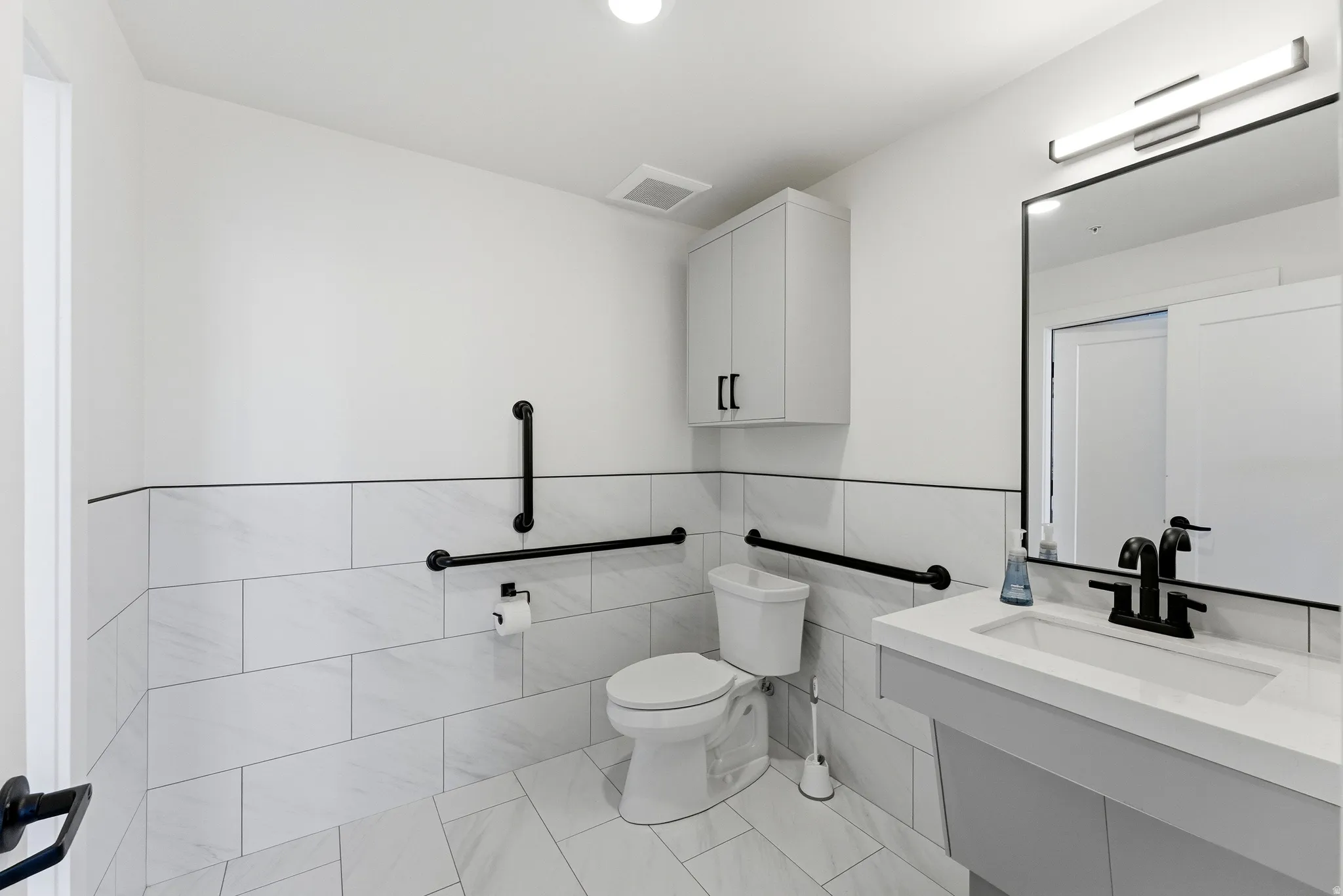 Bathroom with vanity, tile walls, light tile patterned flooring, and a wainscoted wall