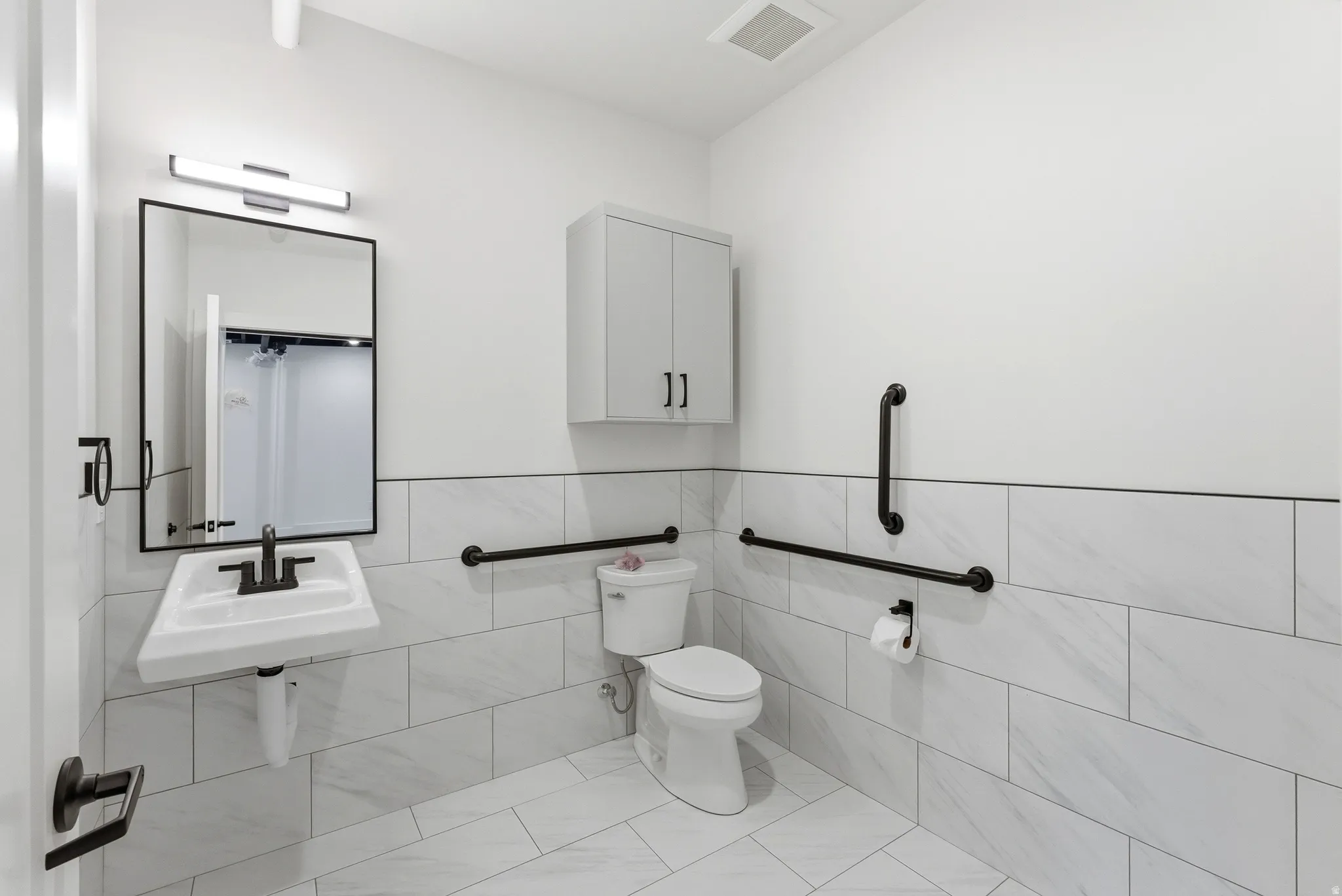 Bathroom with tile walls, light tile patterned floors, and wainscoting