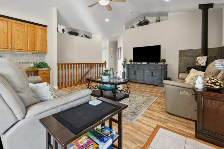 Famly area showing stairs to basement, light wood-style flooring, vaulted ceiling, a wood stove, and plant shelves