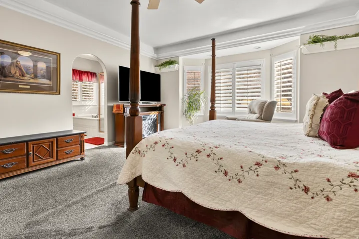 Primary bedroom with carpet flooring, a ceiling fan, multiple windows, connected bathroom, and ceiling rim lighting