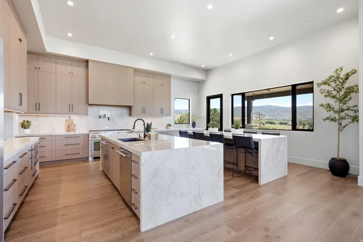 Spacious kitchen featuring two large islands with waterfall countertops, premium stainless steel appliances, extensive cabinetry, and wood-finish flooring