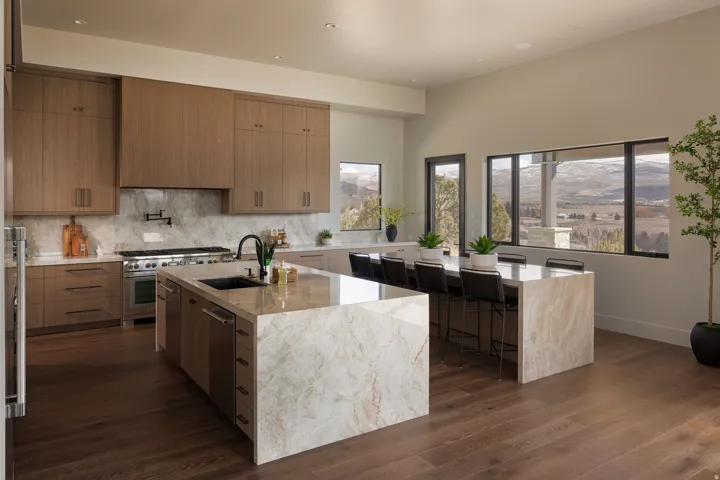 Spacious kitchen featuring two large islands with stone countertops, integrated sink, rich wood-finish flooring, and extensive wood cabinetry