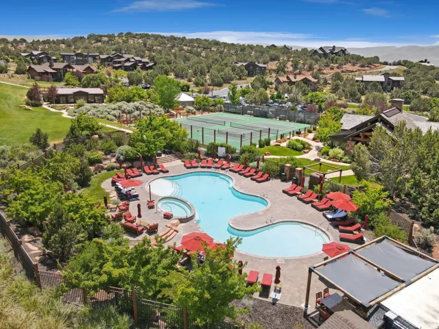 Shaped swimming pool with an integrated spa, expansive pool deck, tennis courts, and landscaped grounds