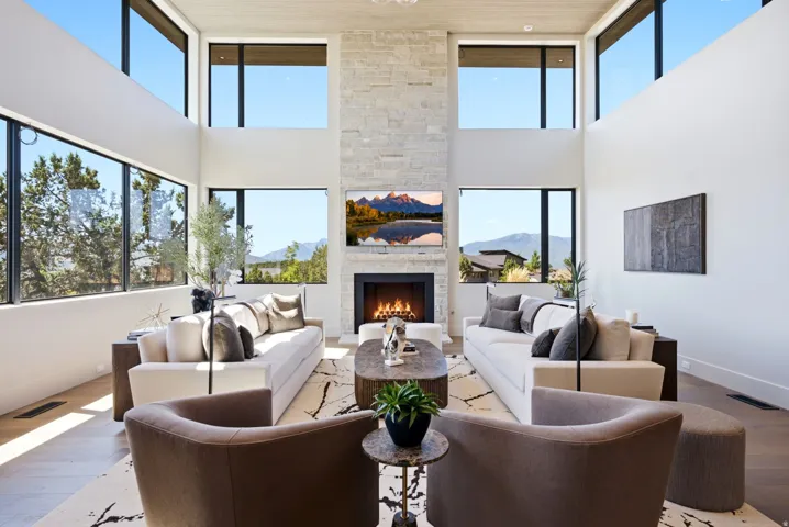 Two-story living area with expansive windows, stone-clad fireplace, and wood-finish flooring