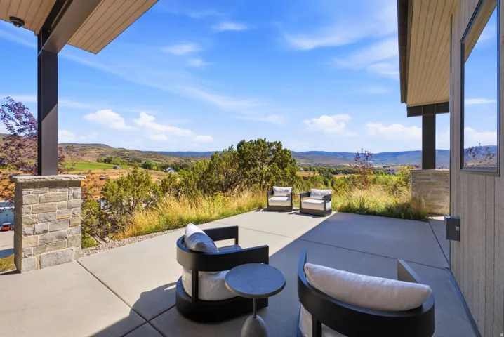 Expansive concrete patio with stone-faced pillars and a wood-finish ceiling, offering a scenic landscape