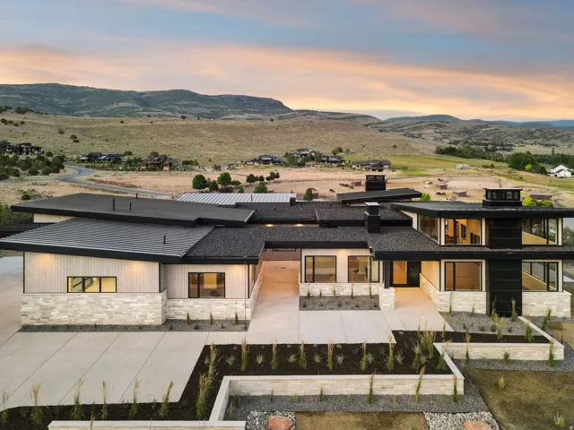 Modern exterior featuring multiple rooflines, stone and wood-look siding, extensive fenestration, and concrete hardscaping