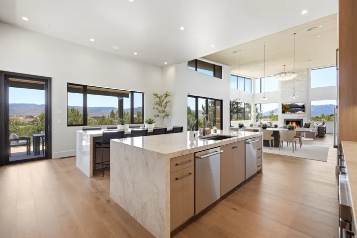 Expansive open-concept living area featuring light wood-finish flooring, a kitchen island with integrated stainless steel appliances, a breakfast bar, and multiple large windows