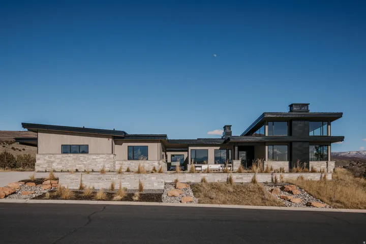 Modern architectural design featuring expansive windows, natural stone veneer, sloped rooflines, and multi-level landscaping
