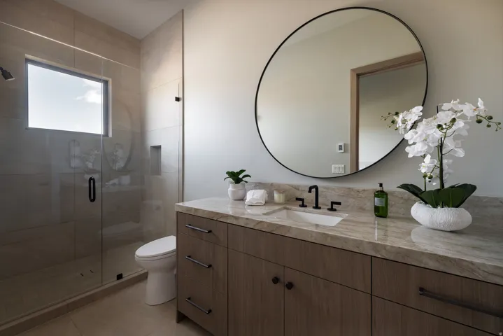 Floating vanity with wood-finish cabinetry, stone countertop, undermount sink, and black fixtures