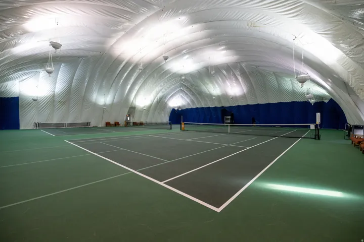 Indoor tennis court with a green playing surface, white court lines, and a dark net