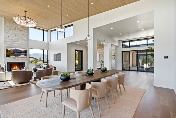 Vaulted ceiling with wood-finish paneling, stone-clad fireplace, large format windows, recessed lighting, and wood-finish flooring
