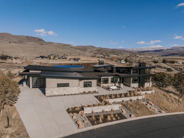 Modern architectural design featuring stacked stone and horizontal siding, extensive paved driveway, solar panels, and a multi-level outdoor patio