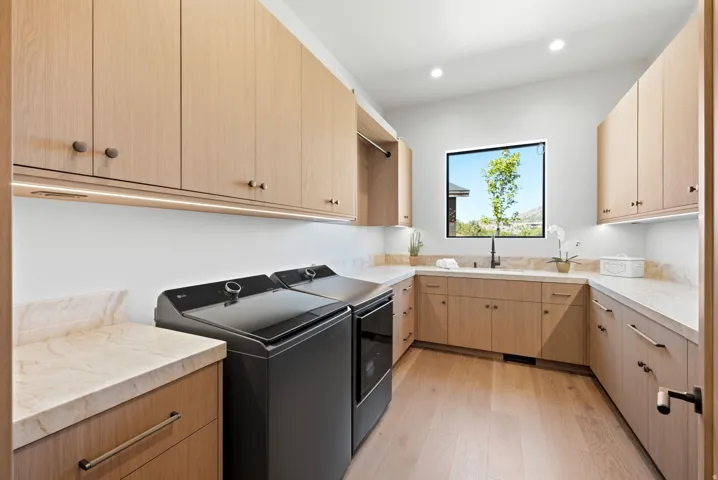 Light wood-finish cabinetry with integrated under-cabinet lighting, light-toned countertop surfaces, and a window with a black frame