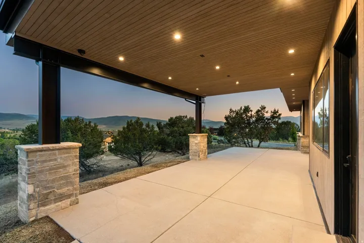 Expansive covered patio with recessed lighting, concrete flooring, stone-clad pillars, and a wood-finish ceiling