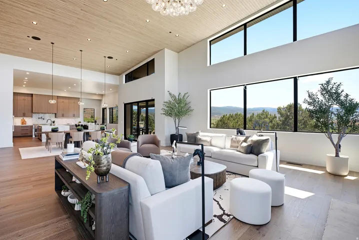High ceilings with wood-finish paneling, expansive floor-to-ceiling windows, modern kitchen featuring integrated appliances, large central island with seating, and wood-finish flooring throughout