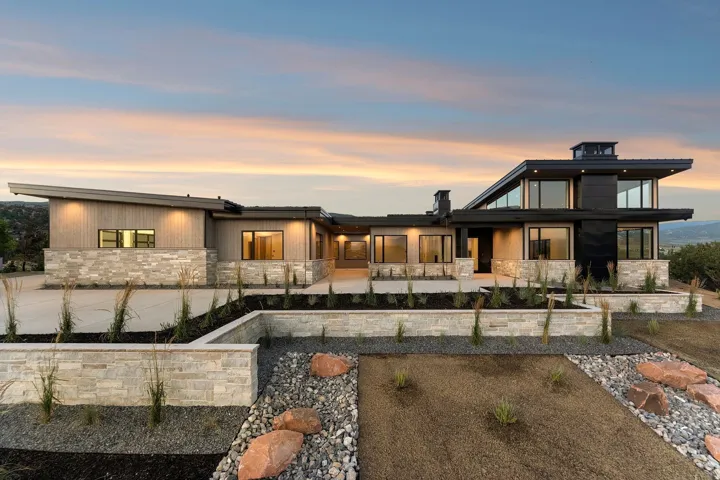 Modern architectural design with a multi-level roofline, stone and wood-finish exterior, expansive windows, and integrated exterior lighting