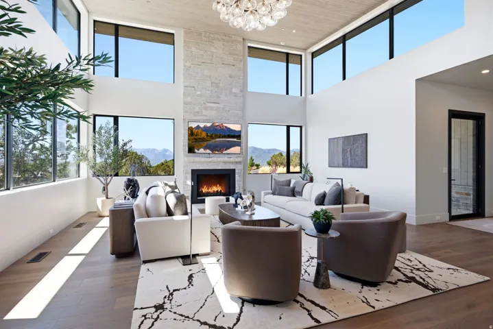 Vaulted ceiling with wood-finish planks, stacked stone fireplace, large format windows, wood-finish flooring, and a contemporary chandelier