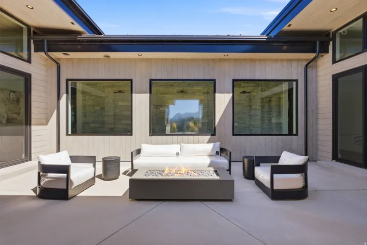 Expansive outdoor patio with concrete flooring, wood-finish paneling, multiple large windows, and an integrated fire feature