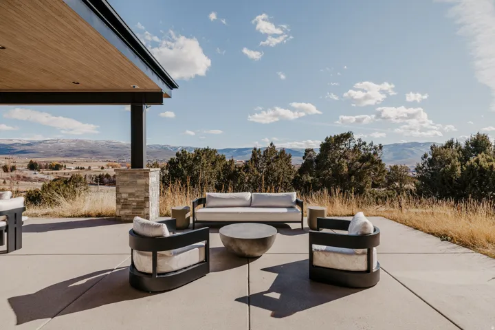 Expansive concrete patio with a covered outdoor area, supported by a stone-clad column and dark structural beams, featuring a wood-finish ceiling