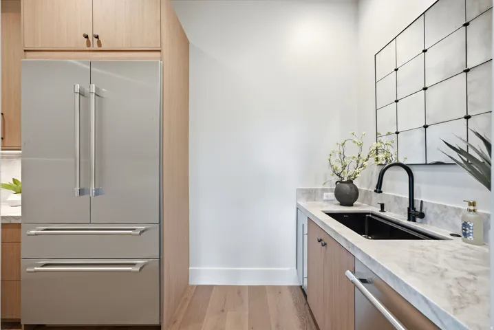 Integrated stainless-steel refrigerator, wood-finish cabinetry, stone countertop, undermount sink with a matte black faucet, and wood-finish flooring