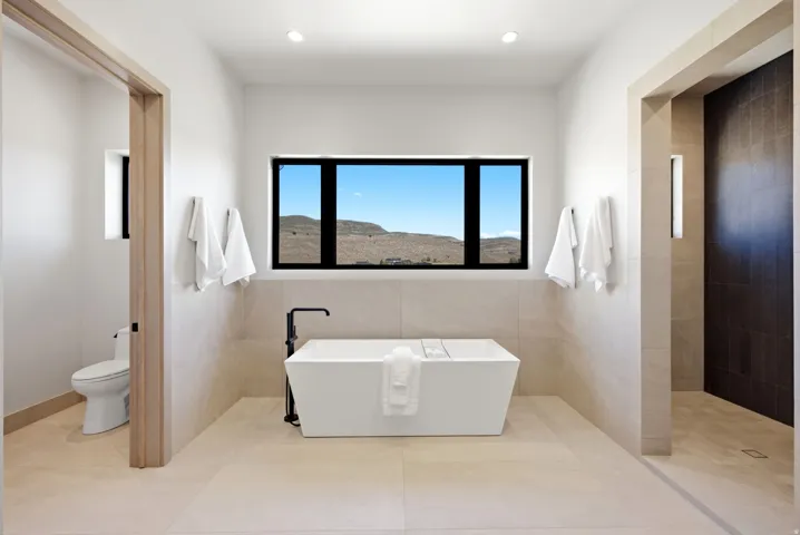 Freestanding soaking tub with a floor-mounted matte black faucet, large format tile flooring, recessed lighting, and a separate walk-in shower with dark tile accents