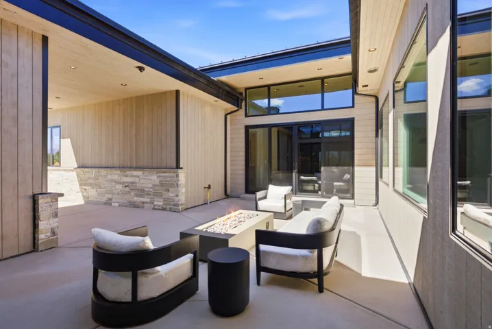 Expansive concrete patio featuring a linear outdoor fire pit, wood-finish siding, and stone accents