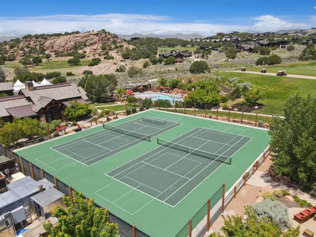 Multiple tennis courts with green hard surfaces and perimeter fencing
