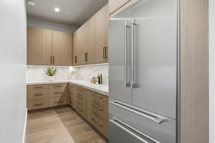 Built-in stainless steel refrigerator, light wood-finish cabinetry, stone countertops, stone backsplash, and recessed lighting