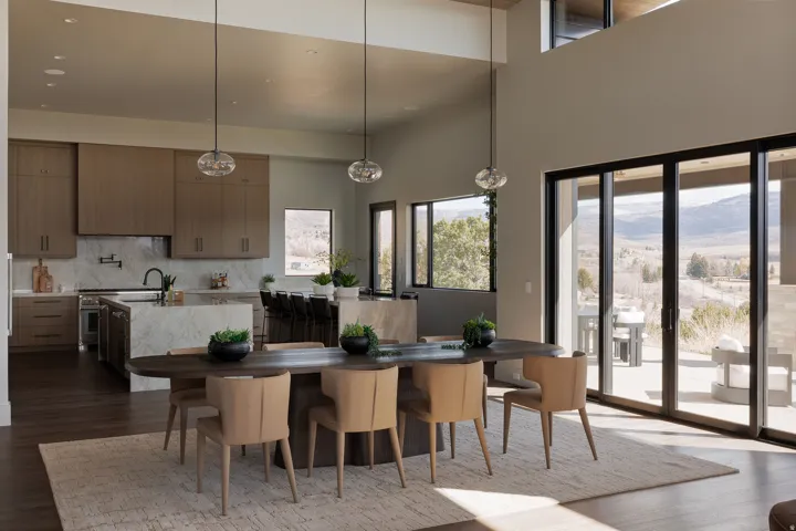 Open-concept living space with high ceilings, wood-finish flooring, a kitchen island with stone waterfall countertop, and an expansive sliding glass door system